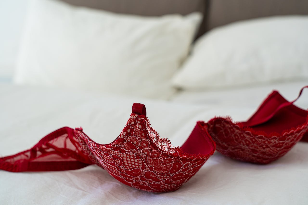 hero-img-01 A red lace bra elegantly laid on a white bed in a stylish bedroom setting.