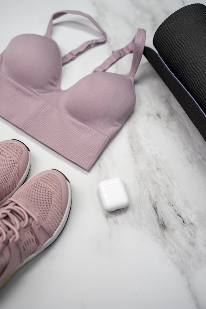 gallery-3 Pastel pink sports bra, sneakers, and yoga mat with earphones on marble.