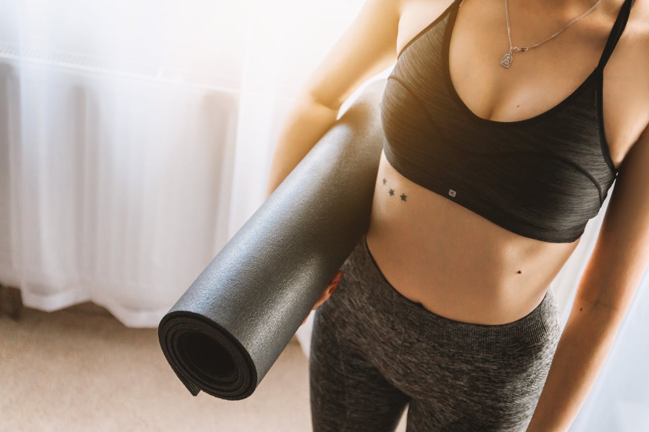 gallery-1 Fit woman in active wear holding yoga mat indoors, ready for workout.